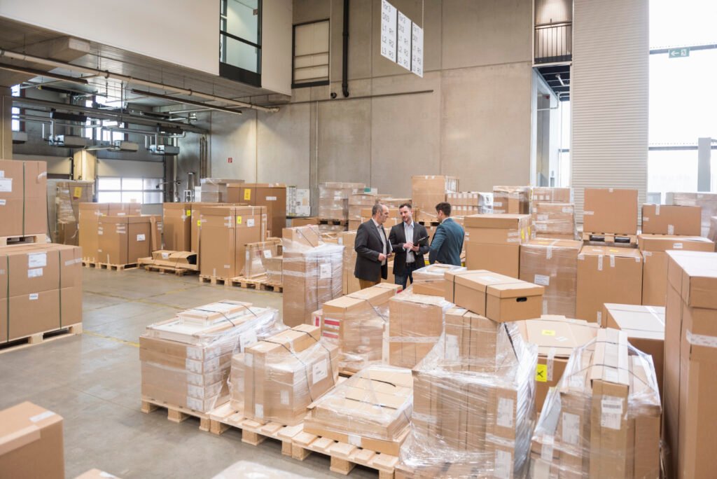 three men in factory warehouse surrounded by cardboard boxes