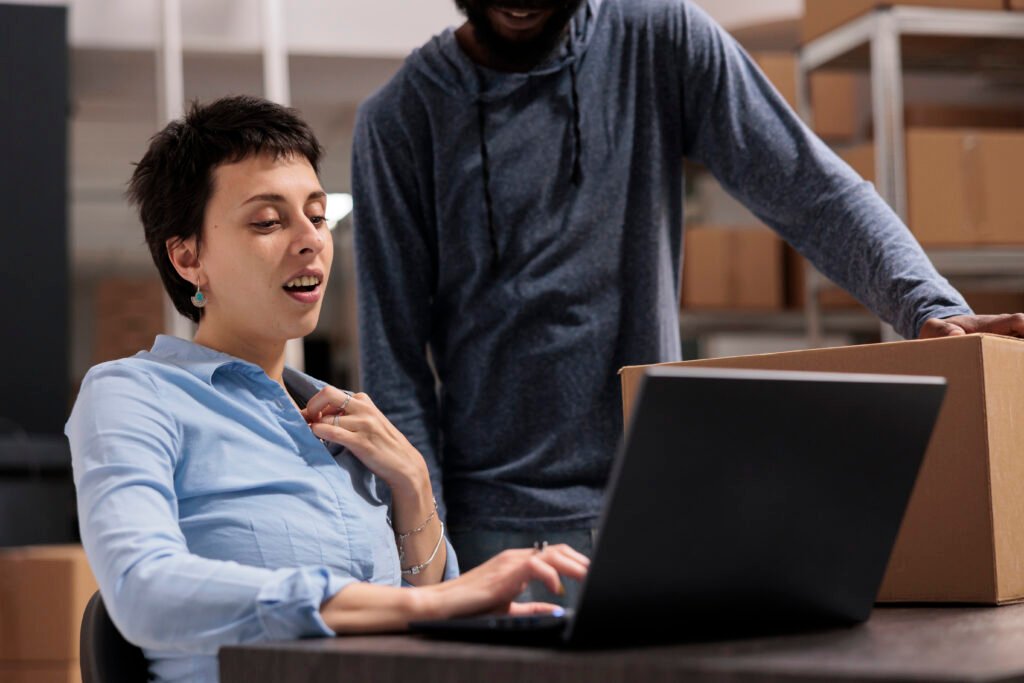 warehouse employees looking at transportation logistics on laptop computer discussing cargo stock