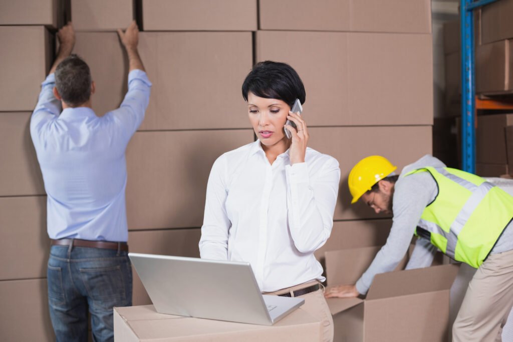 warehouse manager using laptop and talking on phone in a large warehouse